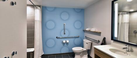 Une salle de bain moderne avec un mur à motifs bleus, des toilettes blanches, un meuble-lavabo en bois et un miroir.