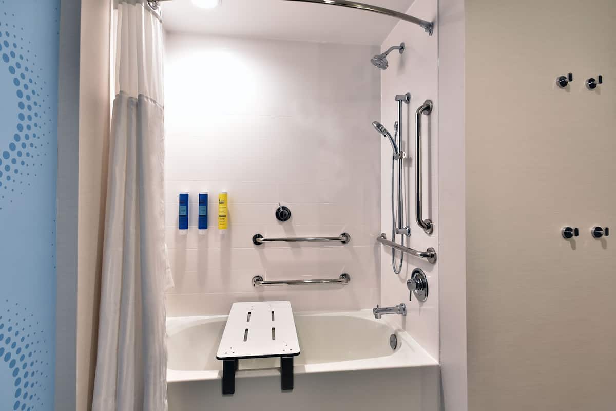 A modern bathroom with a shower, grab bars, and a small bench.