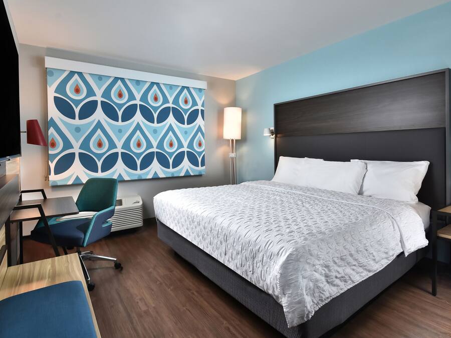 A hotel room with a large bed, a desk with a chair, a TV, and a wall with a geometric pattern.
