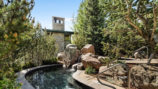 Un jacuzzi rodeado de rocas y árboles, con un edificio de piedra al fondo.