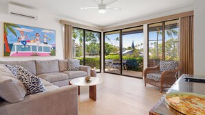A spacious living area with a sofa, armchairs, a coffee table, and a dining table. Large windows provide a view of the outdoors. - Ocean Views and Lots of Turtles - 2 bedroom in Napili (Napili)