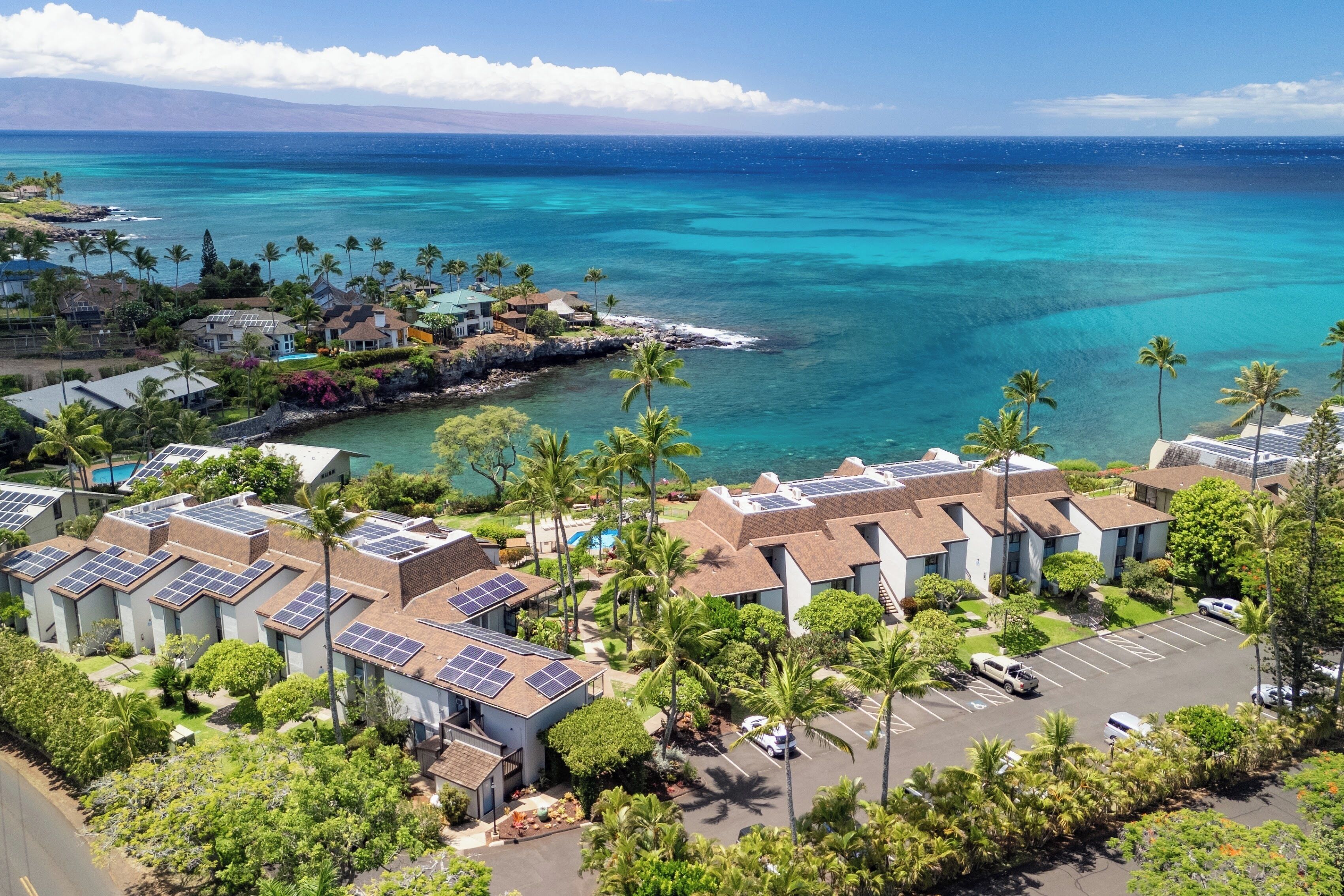 A coastal hotel with multiple buildings, solar panels on rooftops, and a view of the ocean.