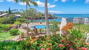 A pool area with lounge chairs, surrounded by tropical plants and palm trees, overlooking a clear blue ocean. - Ocean Views and Lots of Turtles - 2 bedroom in Napili (Napili)