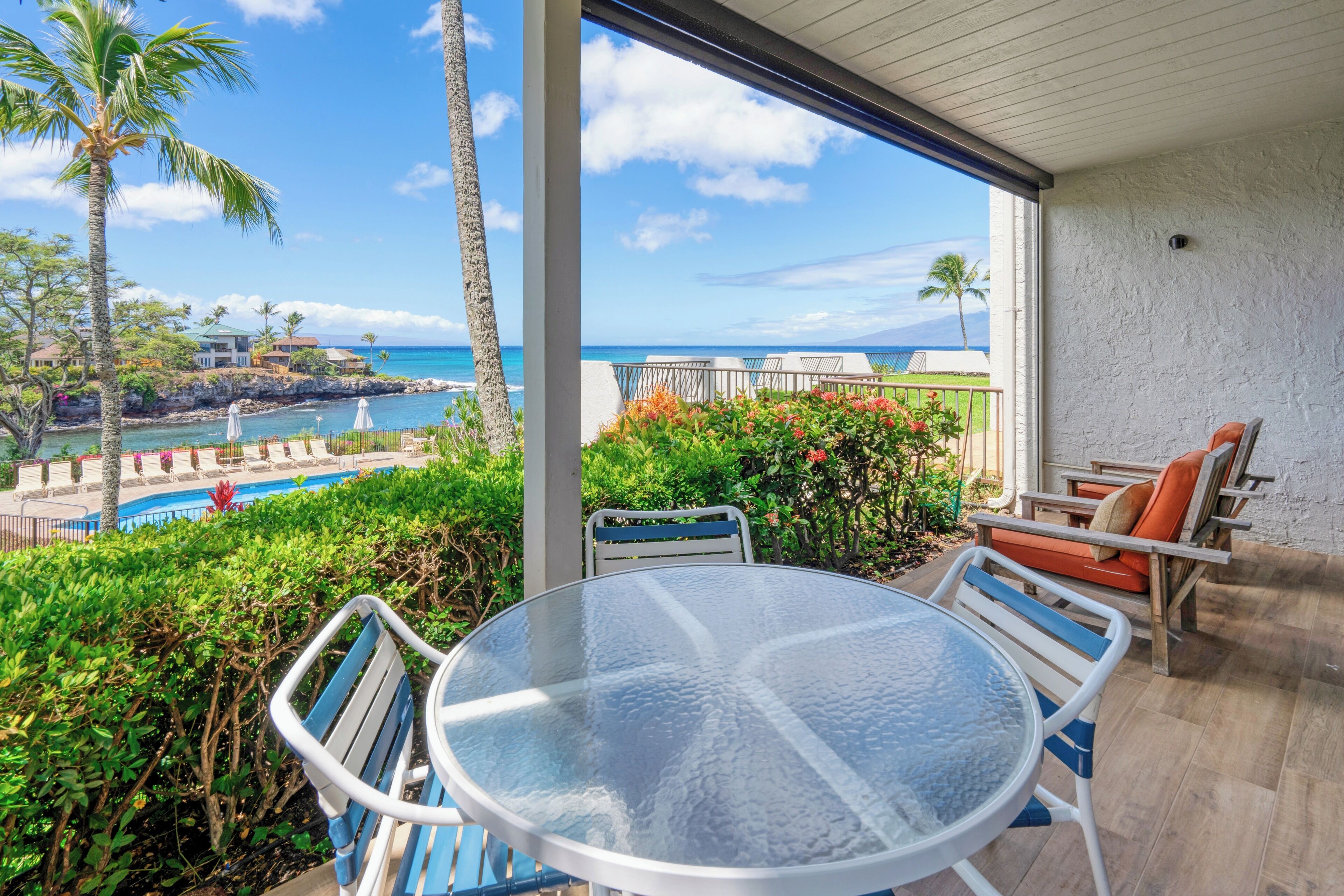 A balcony with a glass table and chairs, overlooking a pool and ocean view.