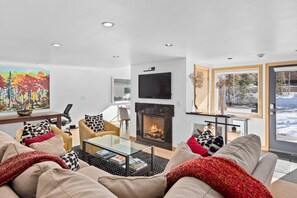 A modern living room with a fireplace, comfortable seating, and a large window with a view of the outdoors.