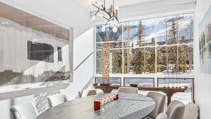 Ett modernt matområde med ett runt bord, grått klädda stolar och ett stort fönster med utsikt över snötäckta träd och berg.