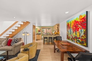 A modern living room with a staircase, a dining area, and a kitchen in the background.