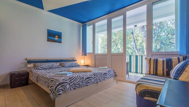 Un dormitorio con una cama, un banco, un ventanal y un cuadro en la pared.