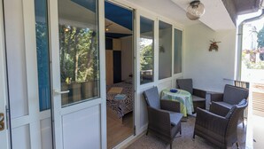 Una habitación con una cama, una pequeña mesa con mantel, sillas de mimbre y vistas a árboles por la ventana.