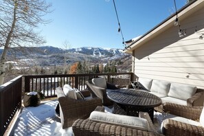 A covered patio with wicker furniture, a round table, and a view of snow-covered mountains. - Lemond Place Home by iTrip Aspen Snowmass (Snowmass Village)