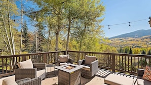 Une terrasse dotée de meubles en osier, d’un foyer extérieur et offrant une vue sur une forêt et des montagnes.