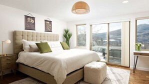 Une chambre à coucher avec un grand lit, une table de chevet, une lampe, une fenêtre avec vue et un luminaire suspendu.