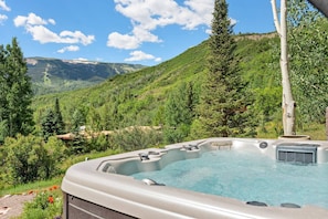 A hot tub with a mountain view, surrounded by lush greenery and trees. - Lemond Place Home by iTrip Aspen Snowmass (Snowmass Village)