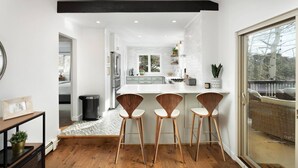 Une cuisine moderne avec des meubles blancs, un îlot central doté de tabourets et une grande fenêtre offrant une vue sur l’extérieur.