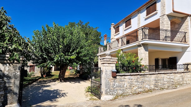 A two-story building with a stone facade, a balcony with black railings, and a clear blue sky. - Apartment Gina (Bale)