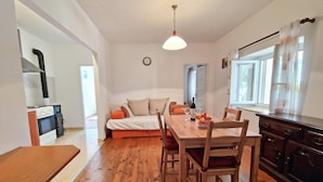 A cozy living room with a wooden dining table, a sofa, and a kitchen area with a stove and cabinets. - Apartment Gina (Bale)