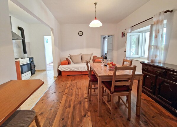 A cozy living room with a wooden dining table, a sofa, and a kitchen area with a stove and cabinets.