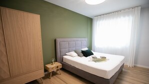 Ein Schlafzimmer mit einem Bett, einem Kleiderschrank, einem Nachttisch und einem Fenster mit Vorhängen.