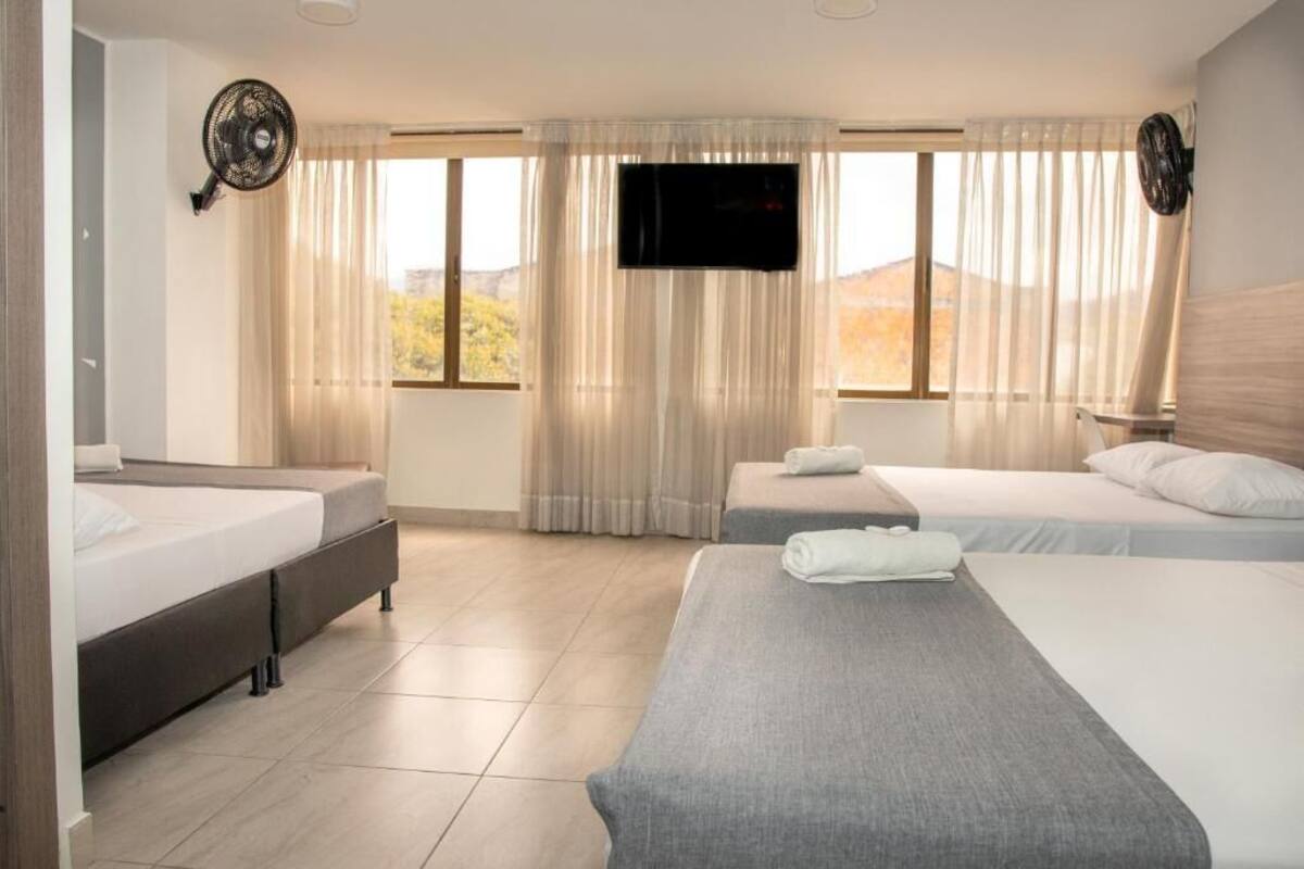 A hotel room with two single beds, a TV mounted on the wall, and a large window with curtains.