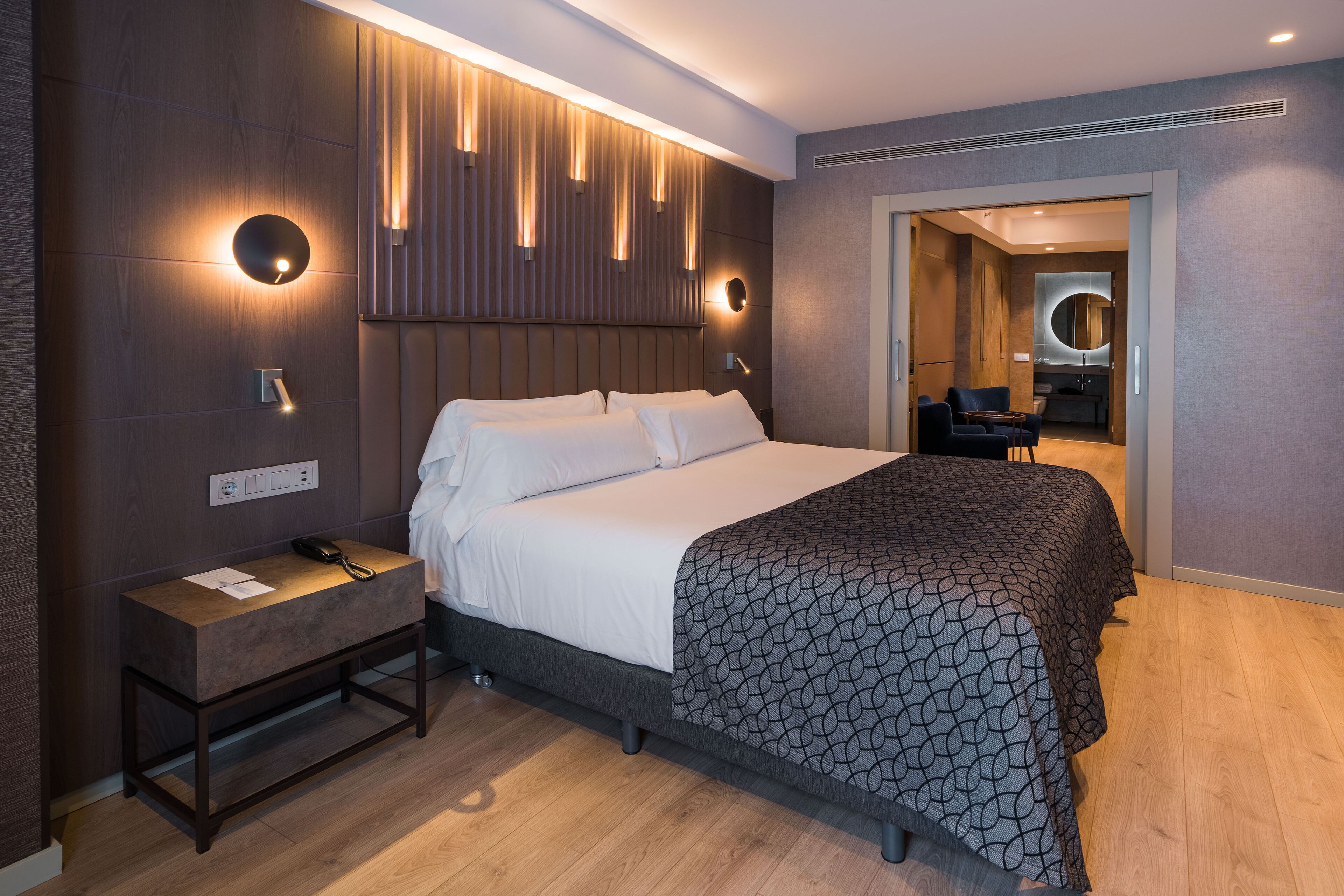 Een moderne hotelkamer met een groot bed, nachtkastje en spiegel.