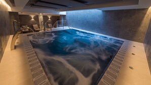 Una piscina interior moderna con fuente, zona de estar e iluminación integrada.