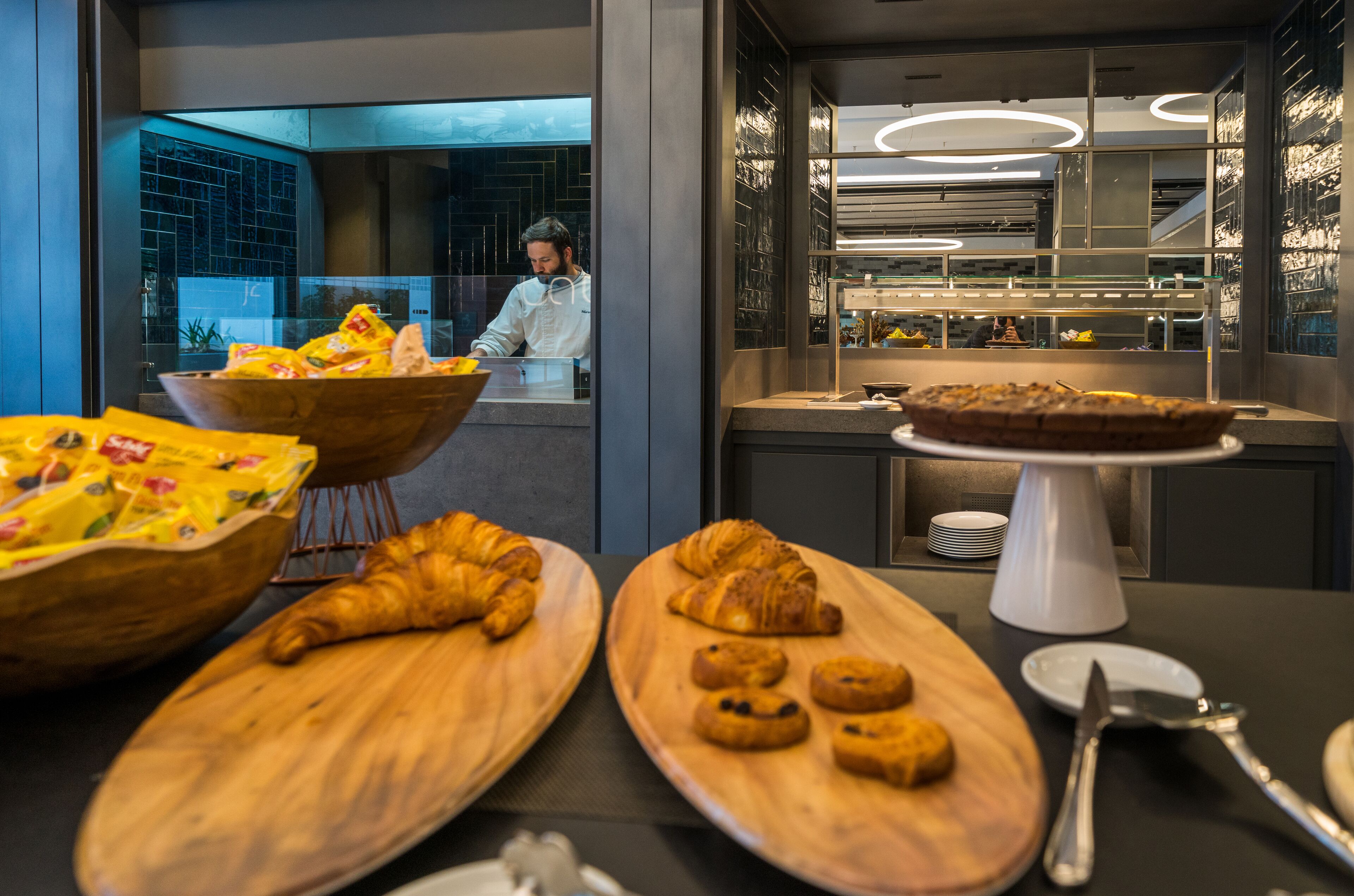 Cocina moderna con tablas de madera que exhiben pasteles y un chef preparando alimentos.