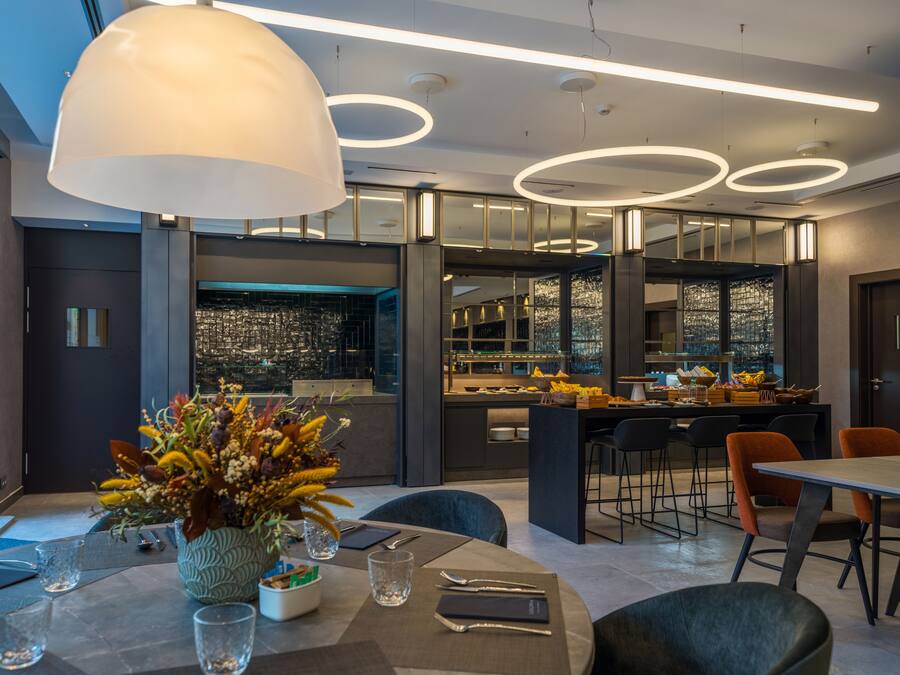 Un restaurant moderne doté d’un bar, de grandes suspensions et offrant une vue sur le paysage urbain.