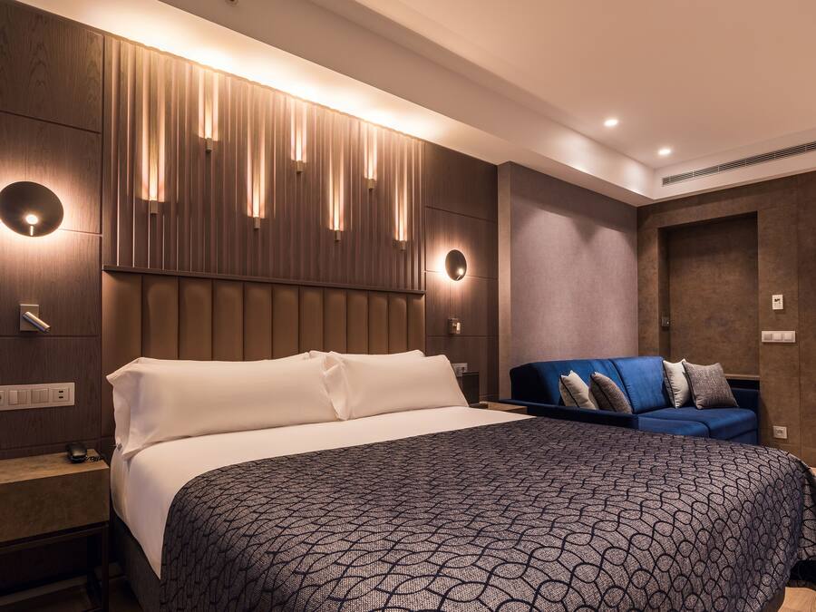 Una habitació d'hotel moderna amb un llit gran, un sofà blau i una làmpada penjada a la paret.