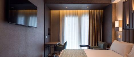 Habitación de hotel con una cama grande, un escritorio, una silla, un televisor montado en la pared y una ventana con cortinas.