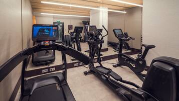 Un gimnasio con varias cintas de correr, elípticas y una pantalla digital que muestra información de los entrenamientos.