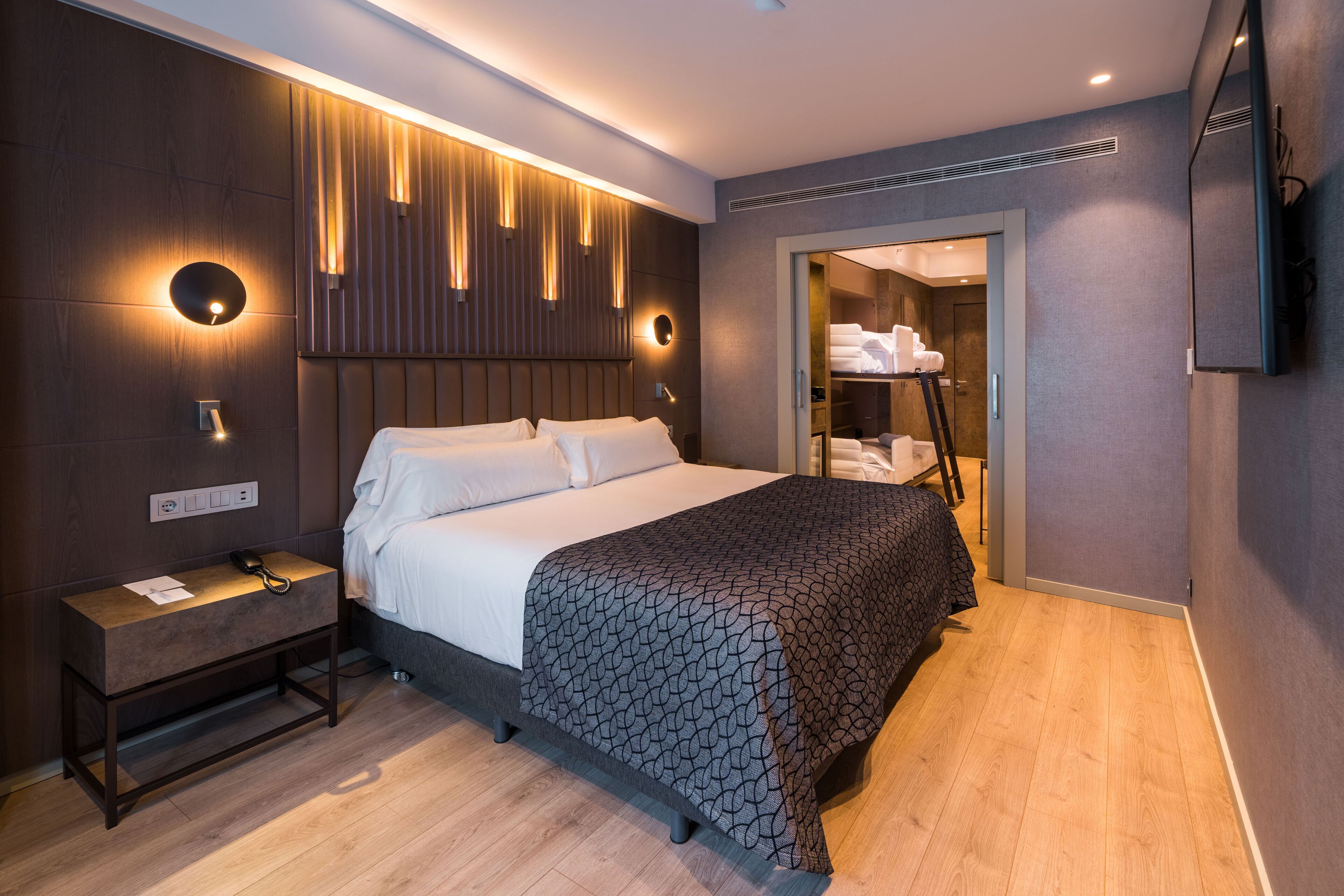 Una habitación de hotel moderna con una cama grande, mesitas de noche, un armario y un espejo.