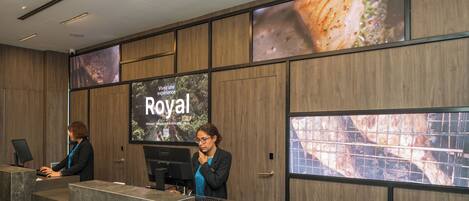 En receptionsdisk med to ansatte, en stor skærm der viser 'Royal'-branding, og et moderne interiør.