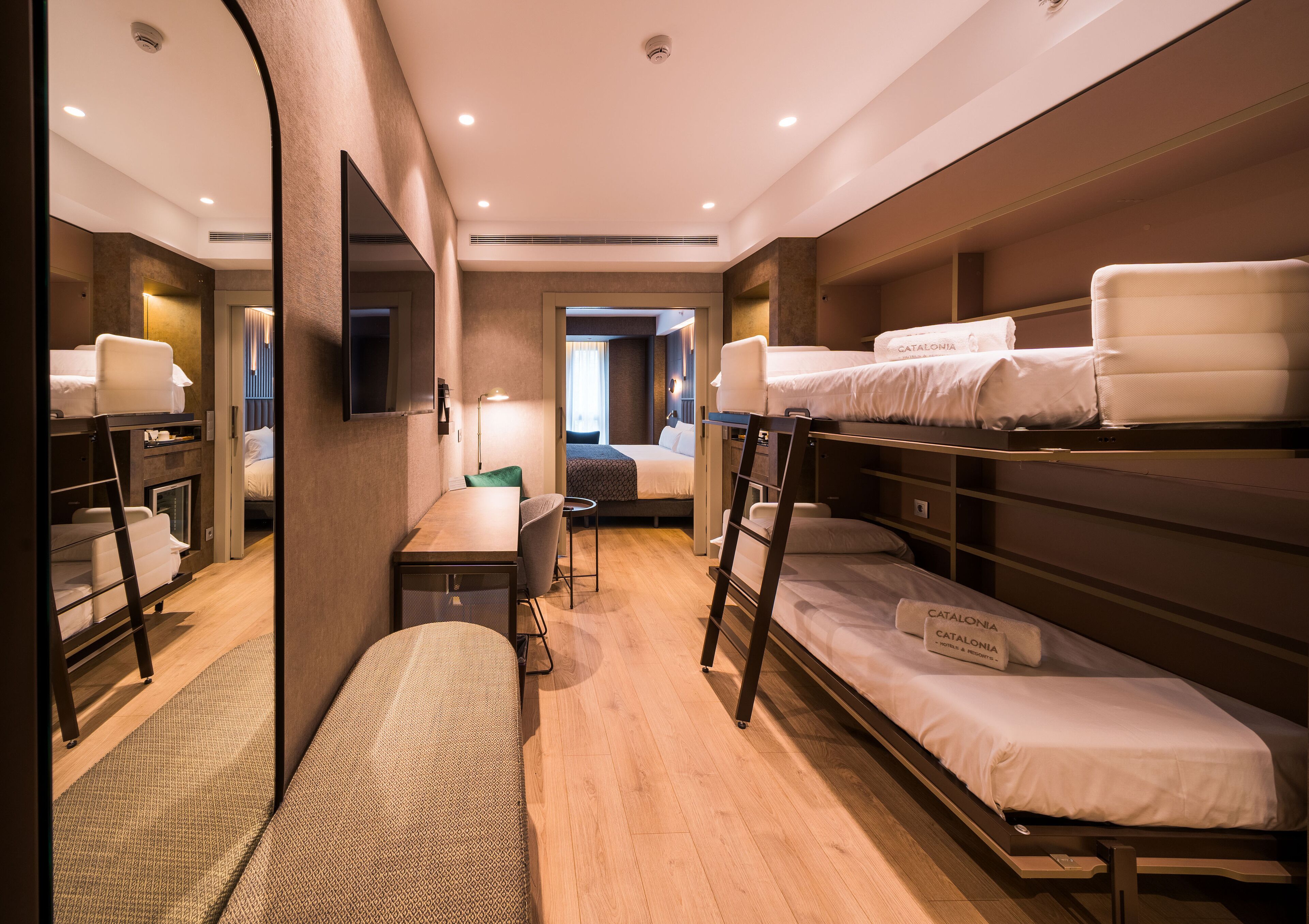 Une chambre d’hôtel équipée de lits superposés, d’un bureau, d’une chaise, d’un téléviseur à écran plat et d’un miroir.