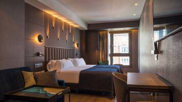 Una habitación de hotel moderna con una cama grande, un sofá, una mesa de comedor y vistas a la ciudad desde la ventana.