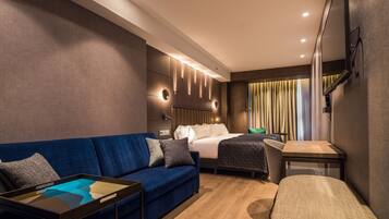 Una habitación de hotel moderna con un sofá azul, una cama, una mesita pequeña y un televisor montado en la pared.