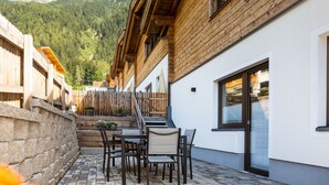 A patio with a table and chairs, a stone wall, and a wooden fence. - Chalet houses (Oetz)