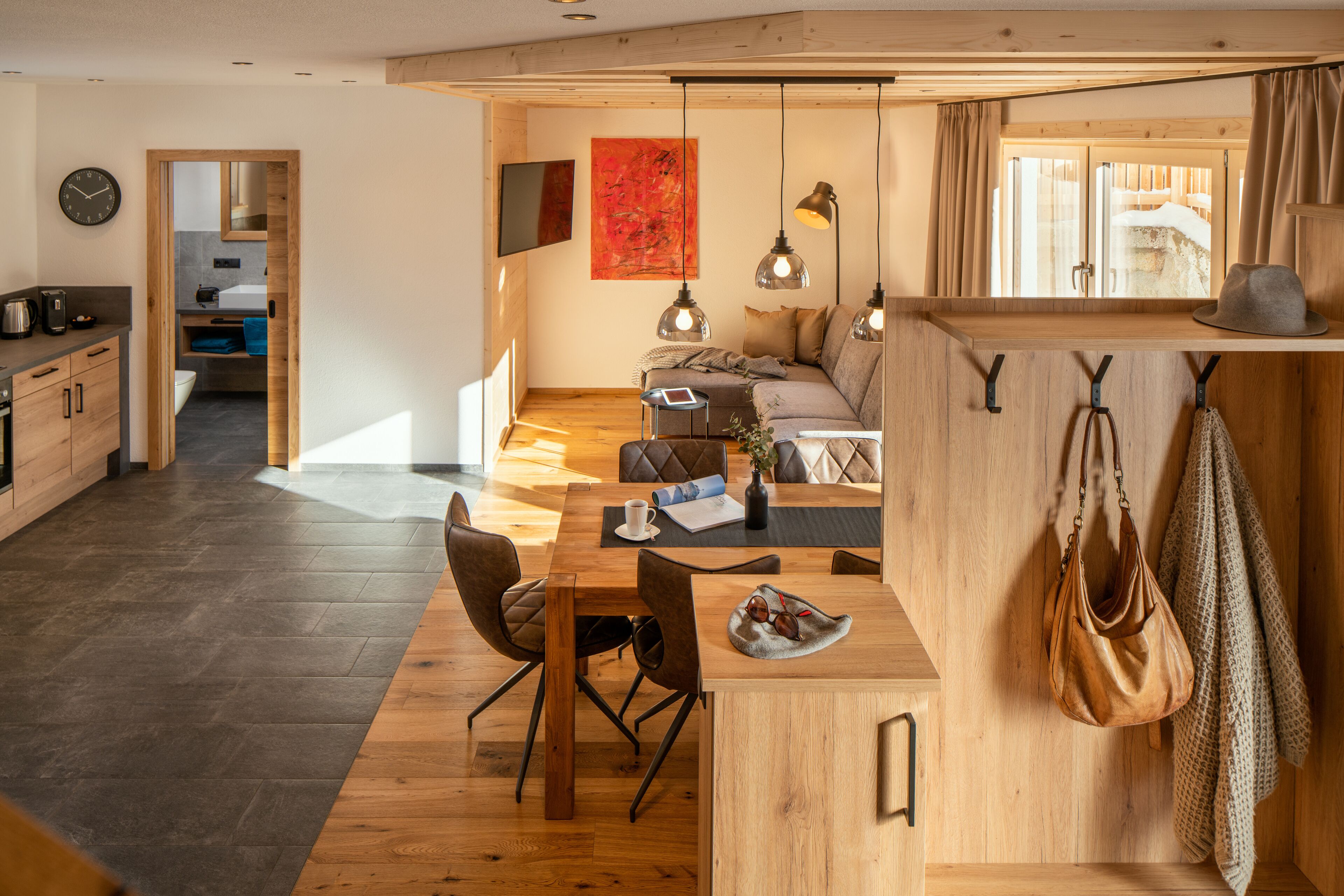 Eine moderne Küche mit Holzausstattung, ein Essbereich mit Tisch und Stühlen sowie ein Wohnbereich mit Sofa und Fernseher.