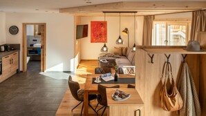 A modern kitchen with wooden cabinets, a dining area with a table and chairs, and a living space with a sofa and a TV. - Chalet houses (Oetz)