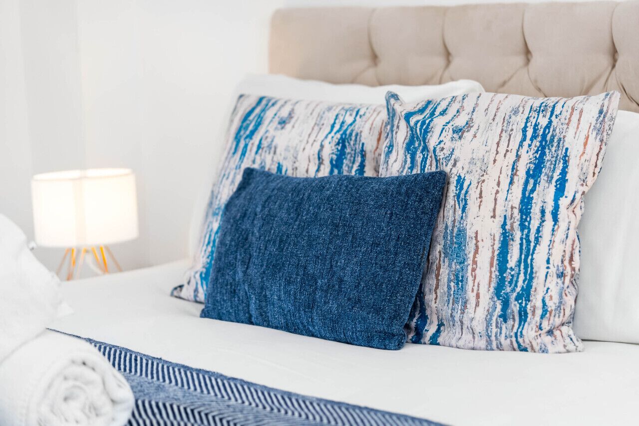 Ein ordentlich bezogenes Bett mit einer weißen Daunendecke, einem blau-weiß gestreiften Kissen und einem dunkelblauen Kissen.