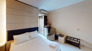 A hotel room with a bed, a desk, a chair, a small fridge, and an air conditioning unit. - Tendean Residence (Jakarta)
