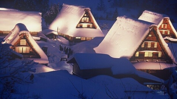 A row of snow-covered cottages with pitched roofs and visible windows, surrounded by snow.