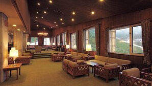 A cozy, well-lit lounge area with wooden furniture, large windows offering scenic views, and a chandelier.
