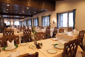 A restaurant with multiple tables set for dining, wooden chairs, and large windows with curtains. - Hotel Tateyama (Tateyama)