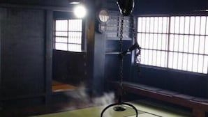 A traditional Japanese room with tatami flooring, a hanging lantern, and a fire pit with burning wood.