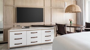 A hotel room with a large flat-screen TV mounted on a wooden panel wall, a dining area with a table and chairs, and a large woven lamp. - BREATHTAKING VIEWS - RITZ CARLTON ST. THOMAS (St Thomas)