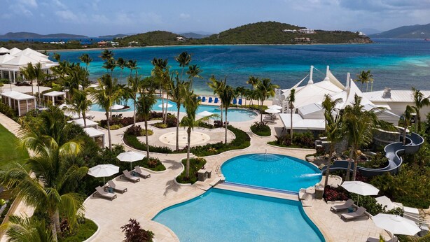 A resort with a large pool, palm trees, and a view of the ocean. - BREATHTAKING VIEWS - RITZ CARLTON ST. THOMAS (St Thomas)