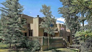 A modern building with a wooden facade, surrounded by dense trees and a grassy area. - Snowmass 2 Bedroom Private Outdoor Hot Tub by iTrip Aspen Snowmass (Snowmass Village)
