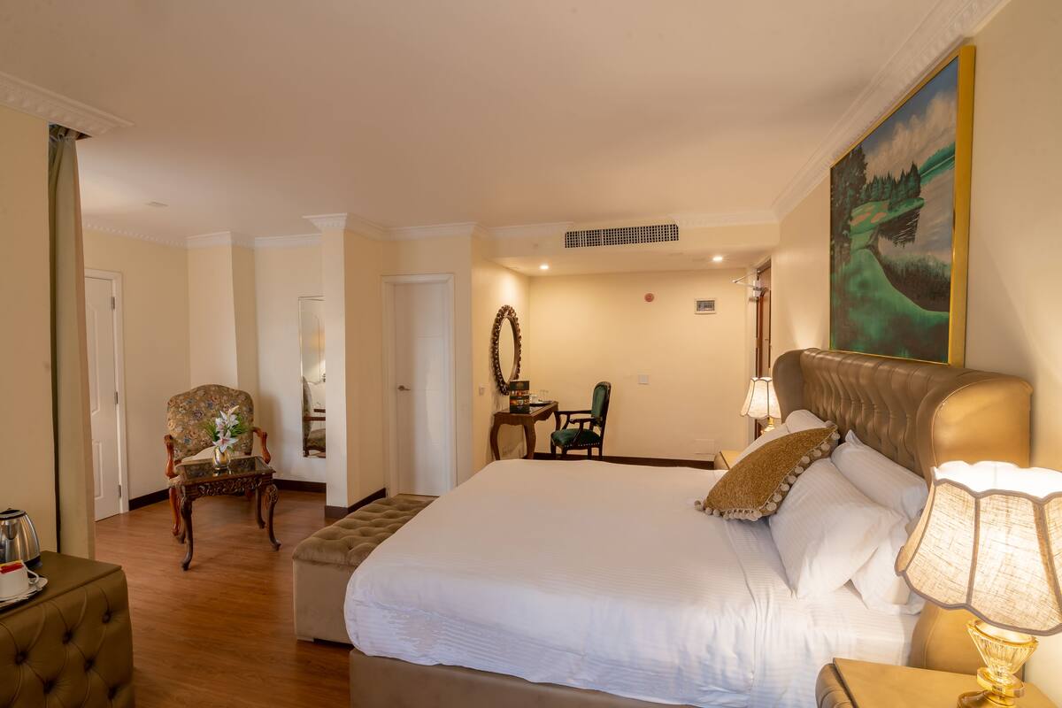 Une chambre d’hôtel avec un grand lit, un coin salon comprenant une chaise et une table, et un tableau accroché au mur.