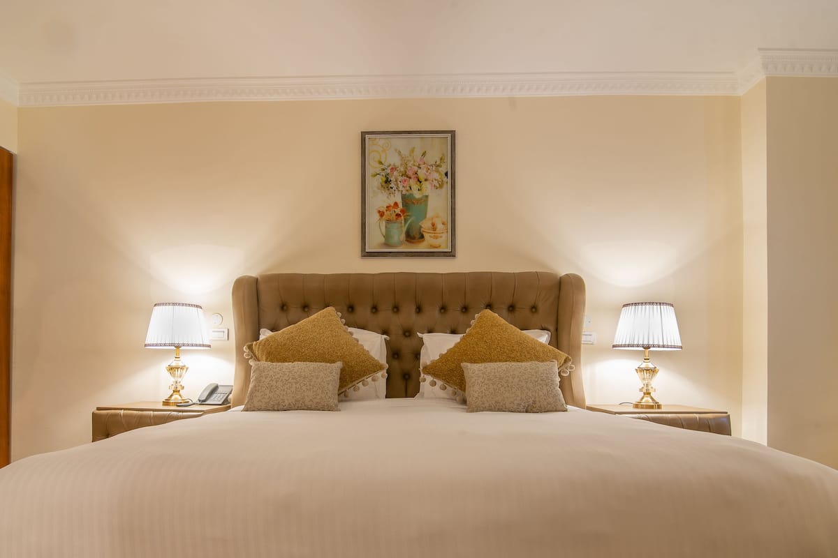 Un grand lit avec une tête de lit capitonnée, deux tables de chevet avec des lampes et un tableau au mur.