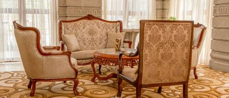 Una habitación con muebles ornamentados, incluyendo un sofá y sillas con estampado, una pequeña mesa redonda y un tapiz decorativo en el suelo.